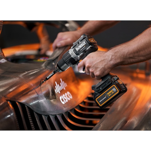 A DEWALT cordless drill is being used on a carbon fiber car part with Cisco branding visible.