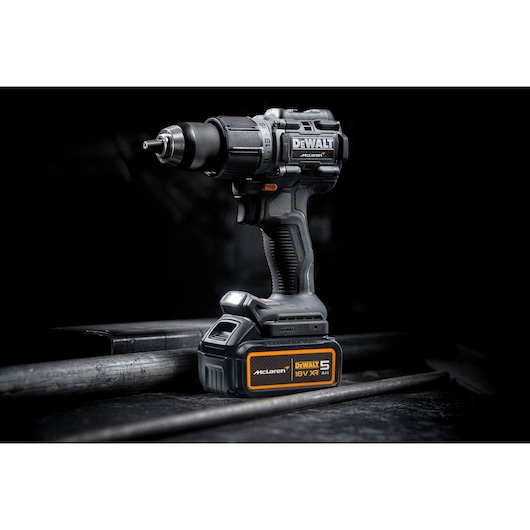 DEWALT 18V XR cordless drill with McLaren branding, resting on a metal surface in a dark studio setting.