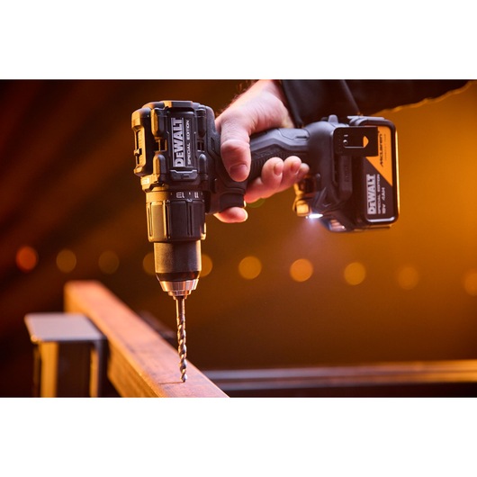 DEWALT cordless drill in use, drilling into metal beam with a bright light and orange background.