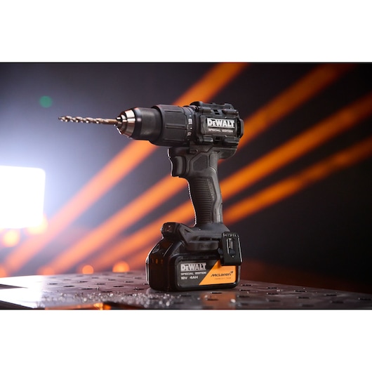 DEWALT cordless drill with McLaren logo, placed on a metal surface, orange light beams in the background.