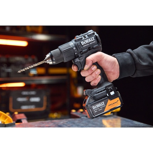A hand holds a DEWALT cordless drill with a drill bit attached, shown in a workshop setting.