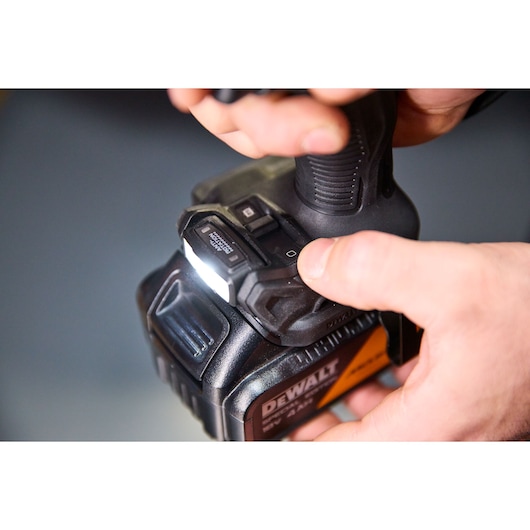 Close-up of hands operating a DEWALT power tool with a lit LED indicator and visible control buttons.