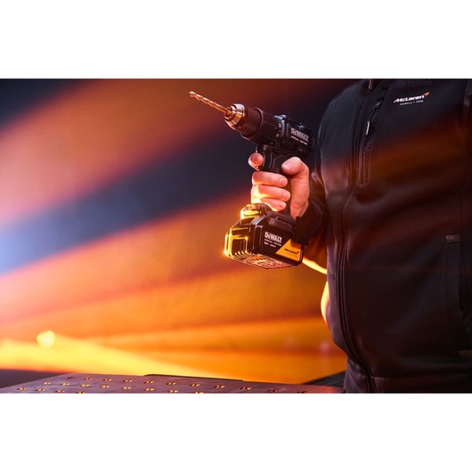 Person holding a DEWALT cordless drill with a drill bit, with an orange light in the background.