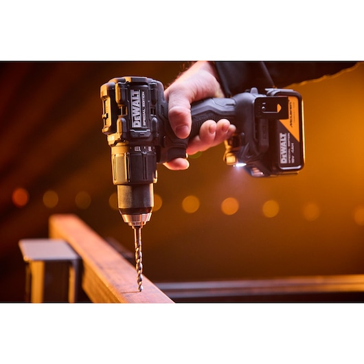 A DEWALT cordless drill is used to drill into a metal beam under warm lighting.