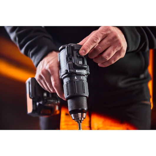 A person adjusts a DEWALT cordless drill, close-up view of hands and tool with an orange background.