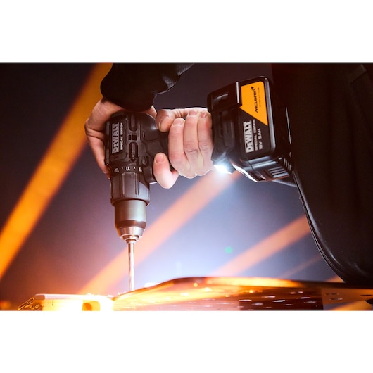 Hand using DEWALT cordless drill to drill into a surface with bright orange light beams in the background.