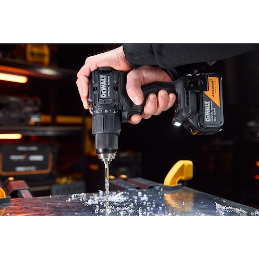 Hand using a DEWALT cordless drill to drill into a metal surface with scattered metal shavings.