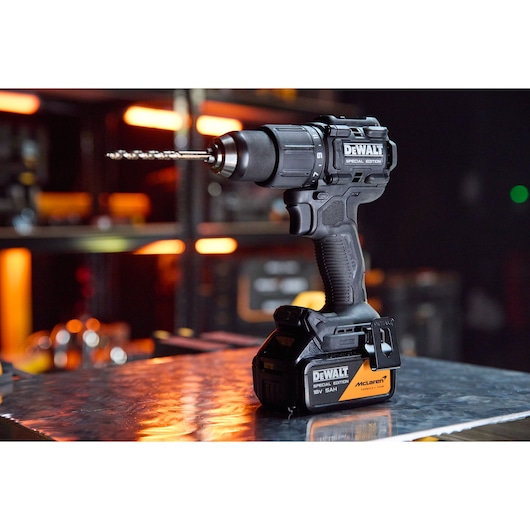 DEWALT cordless drill with McLaren branding on a metal surface, tool shelves with orange lights in background.