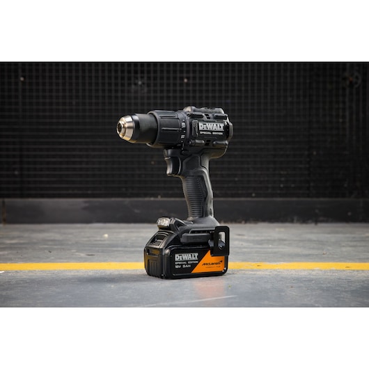 DEWALT cordless drill standing upright on a concrete floor next to a yellow line in front of a dark background.