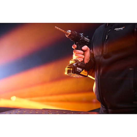 Person holding a DEWALT cordless drill with a bit, set against an orange light background.