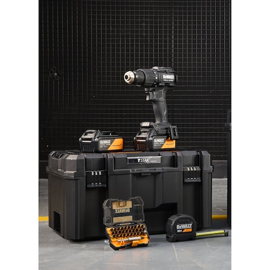 DEWALT cordless drill kit with batteries, tool case, bit set and tape measure shown in front of a black grid wall.