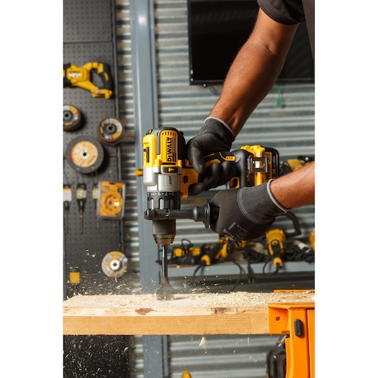 Person uses DEWALT cordless drill to bore a hole in wood, creating sawdust in a workshop setting.