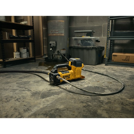 A yellow and black DEWALT portable cordless water transfer pump (model DCE050N) with attached hose is placed on a concrete floor in a workshop or utility room, surrounded by shelves and storage containers.