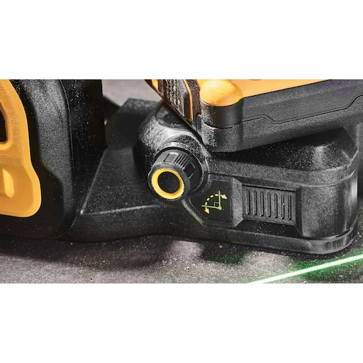 Close-up view of a DEWALT DCE089D1G18 laser level showing the adjustment knob and indicator symbol on the black and yellow casing. A green laser line is visible on the surface below.