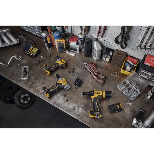 A workbench with a variety of DEWALT power tools, including drill drivers and batteries, surrounded by screws, nails, hand tools, and workshop supplies.