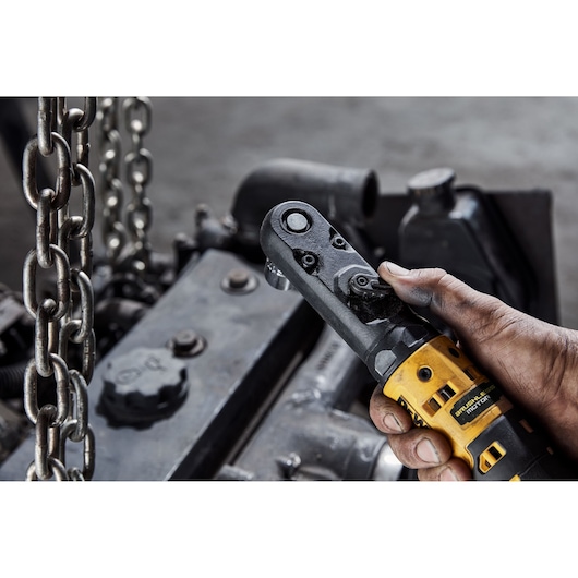 A close-up of a person's hand holding a DEWALT cordless ratchet tool, working near metal chains and machinery parts.