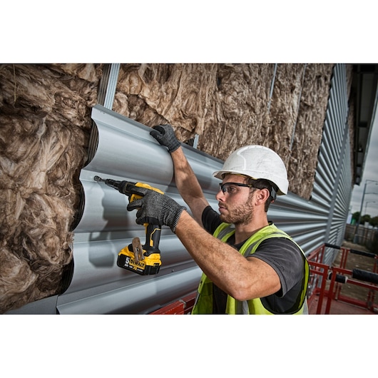 Worker using a DEWALT DCF622P2 cordless screwdriver to install metal siding panels on an insulated wall.