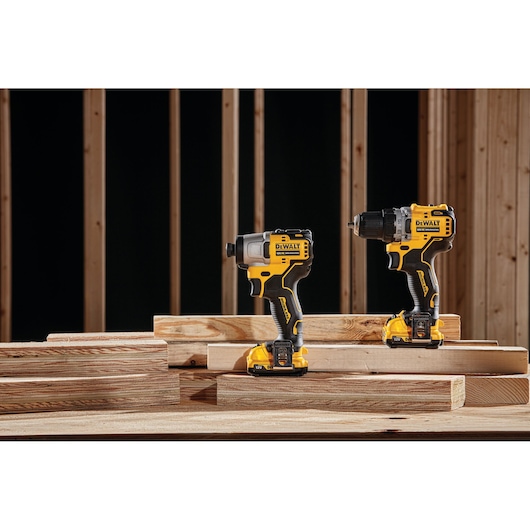 DEWALT power tools DCK2111L2T-XE and DCF801N displayed on wooden planks at a construction site.