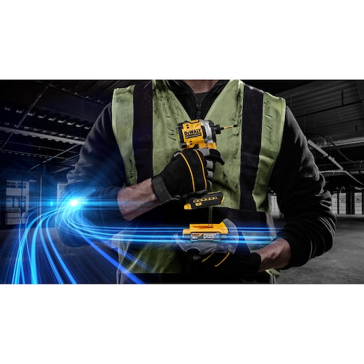 Person holding a DEWALT DCF850E1T impact driver with gloves and safety vest, blue light streaks in industrial setting.