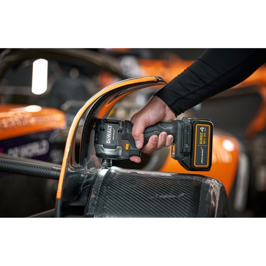 A person uses a DEWALT cordless power tool to work on the carbon fiber body of an orange and black racing car.