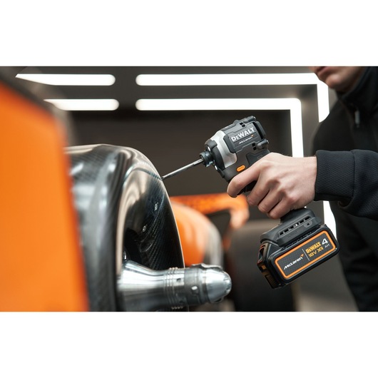 A person using a DEWALT cordless impact driver to work on a metallic and carbon fiber component, with close-up view of the tool and battery.