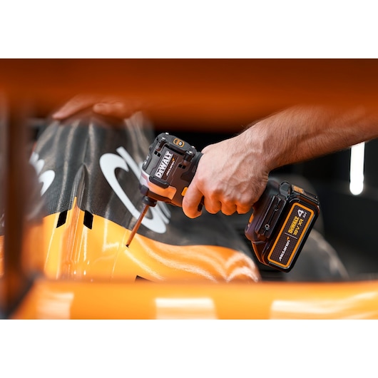 A close-up of a person using a DEWALT cordless impact driver on an orange and black surface.
