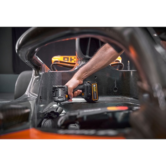 A person's hand holding a DEWALT cordless tool inside a carbon fiber structure, possibly part of a racing car cockpit.