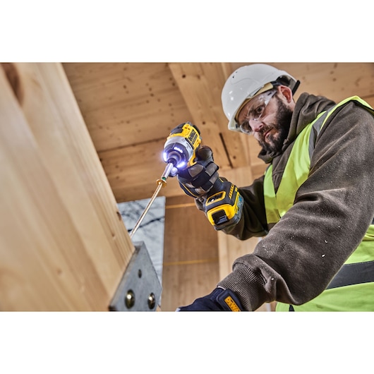 Worker uses DEWALT DCF860E2T impact driver to fasten screws into wooden beams at a construction site.