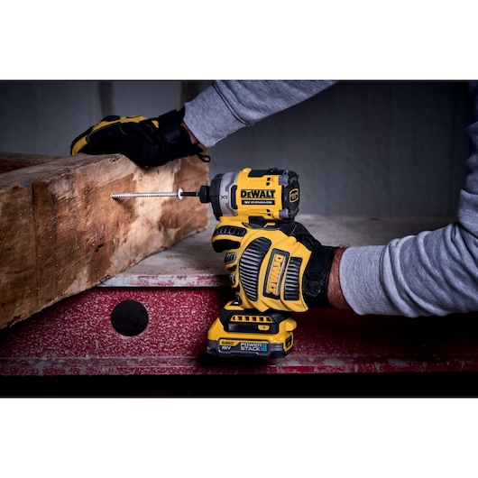 Person using DEWALT DCF860N impact driver to insert a screw into a wooden beam.