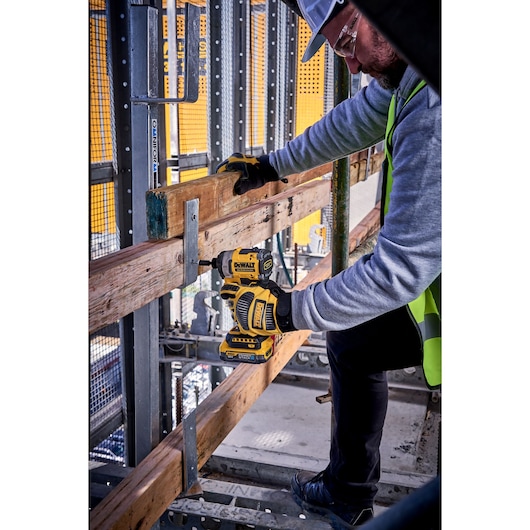 Worker uses DEWALT DCF860N impact driver to fasten wooden beams on construction site.