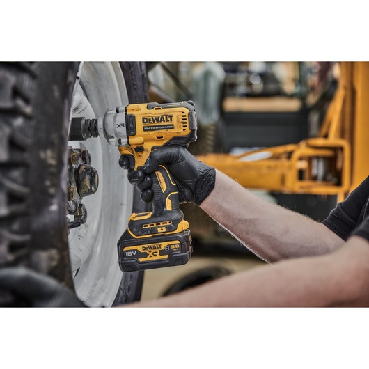 A person wearing black gloves uses a DEWALT DCF891NT cordless impact wrench to tighten or loosen bolts on a large vehicle wheel.