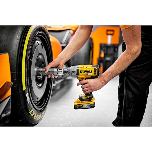 A person is using a DEWALT cordless impact wrench (model DCF900H2T) to work on the wheel of a racing car.