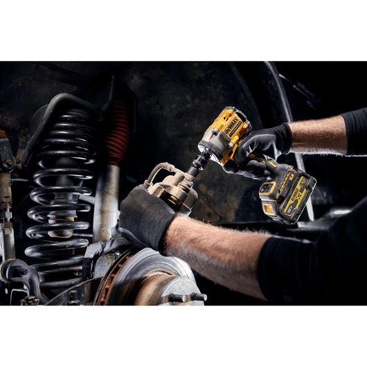 A person wearing black gloves is using a yellow DEWALT cordless impact wrench to work on the suspension and brake system of a vehicle.