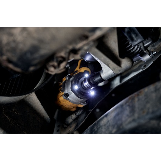 A DEWALT DCF923P2G cordless impact wrench in use, tightening or loosening a bolt in a vehicle's suspension area, illuminated by built-in LED lights.