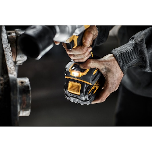 Close-up view of a person holding a DEWALT 18V cordless power tool, focusing on the tool's battery and LED indicator in a workshop setting.