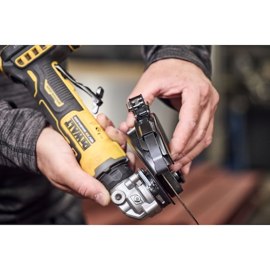 Hands attach a guard to a yellow DEWALT angle grinder. Close-up view of tool assembly in progress.