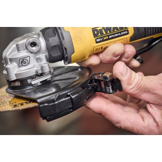 Hand adjusts guard on yellow DEWALT 18V XR brushless angle grinder in close-up view.