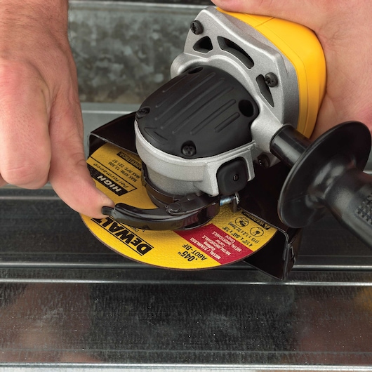 Close-up of a DEWALT angle grinder being adjusted by hand on a metal surface.