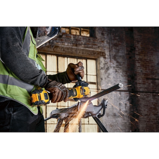 A DEWALT cordless grinder cutting metal, with sparks flying, operated by a worker in safety gear.
