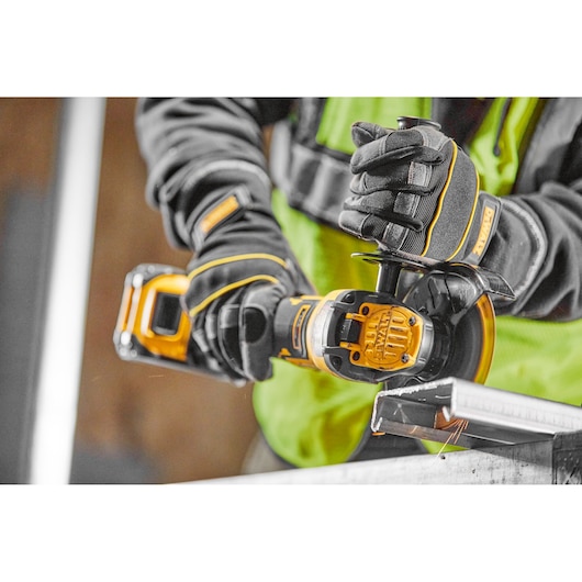 Worker uses a DEWALT cordless angle grinder to cut metal, wearing gloves and safety gear.