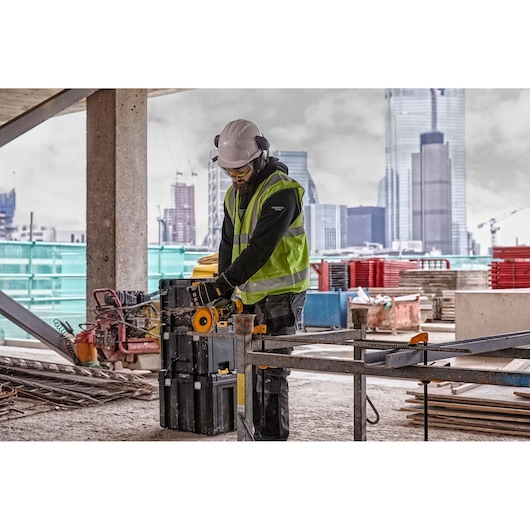 DEWALT tools DCZ507T2-XE, DCG418N, DCZ503X2-XE in use on construction site, worker cutting metal, urban backdrop.