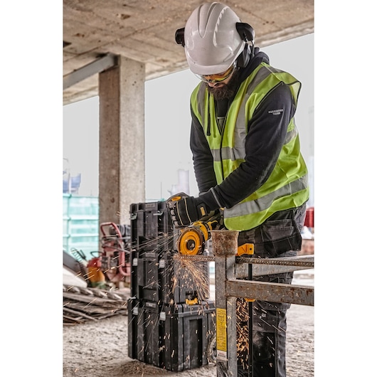 DEWALT DCZ507T2-XE, DCG418N, DCZ503X2-XE tools in use on site. Worker cuts metal; safety gear and sparks visible.