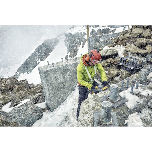 Outdoor snowy worksite with DEWALT DCZ507T2-XE, DCG418N, DCZ503X2-XE tools used for construction among rocks.