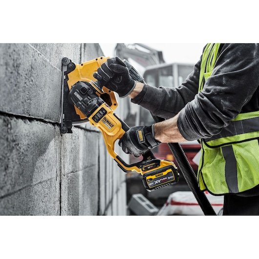 Person using DEWALT cordless wall chaser tool to cut grooves in concrete blocks at a construction site.