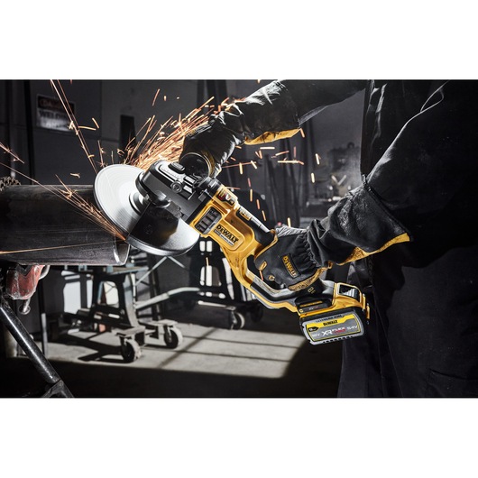 DEWALT cordless angle grinder cutting metal pipe, sparks flying in workshop setting.