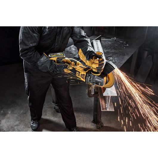 Person using a DEWALT angle grinder, producing sparks while cutting metal in an industrial workshop.
