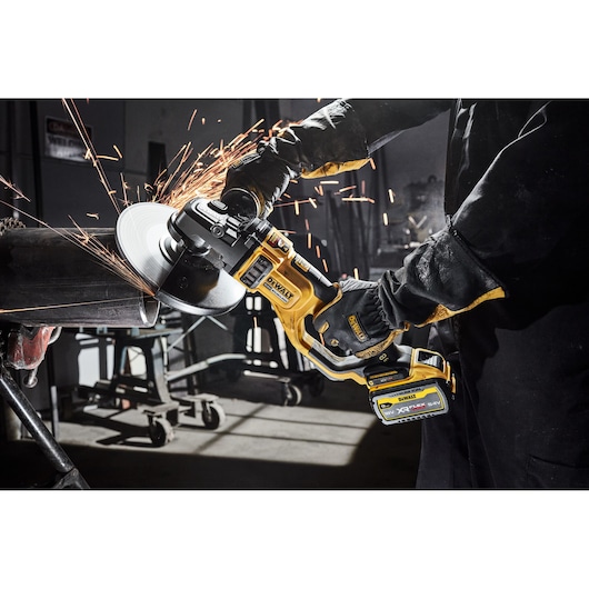 Person using a DEWALT cordless grinder, cutting metal pipe with sparks flying in a workshop.