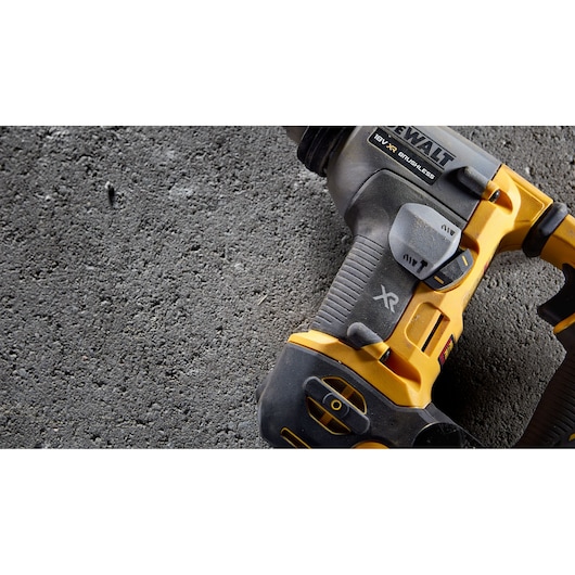 Close-up of a DEWALT 18V XR brushless rotary hammer drill placed on a rough concrete surface.