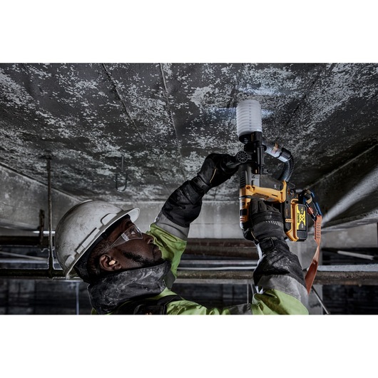Worker uses DEWALT DCH172P2 rotary hammer drill on a ceiling, wearing safety gear in an industrial setting.