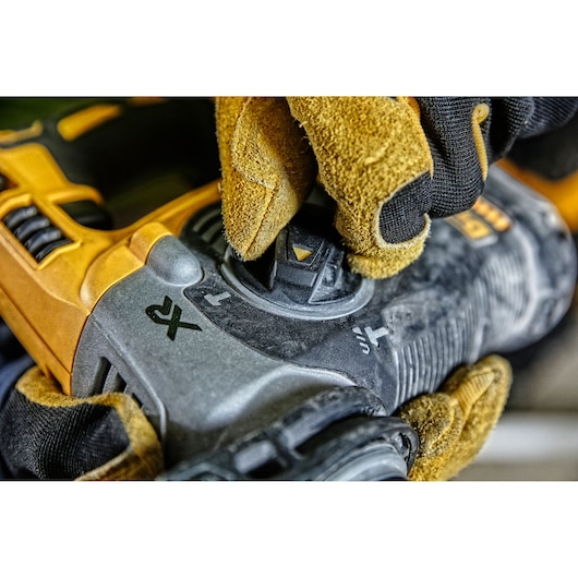Gloved hand adjusting the mode selector on a DEWALT power tool, close-up view of dial and tool details.